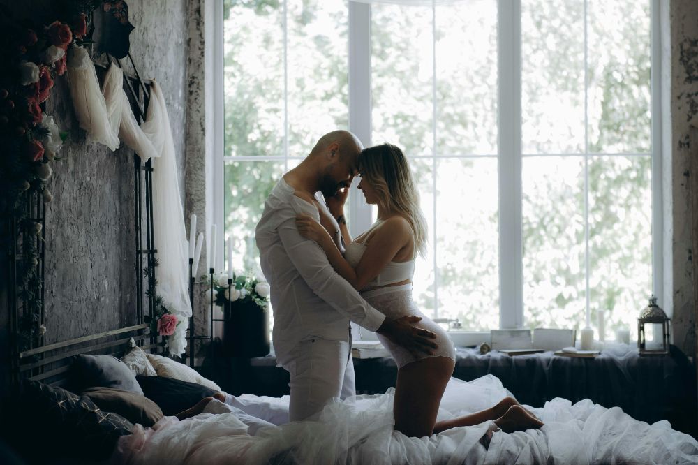 Couple kneeling on bed, embracing intimately and smiling